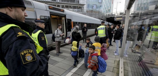 Policisté a skupina migrantů na vlakovém nástupišti ve Švédsku.