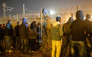 Uprchlíci ve francouzském Calais přelézající plot.