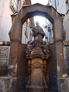 Barokní socha svatého Jana Nepomuckého v kubistickém přístřešku sousedního paláce Diamant v Praze.