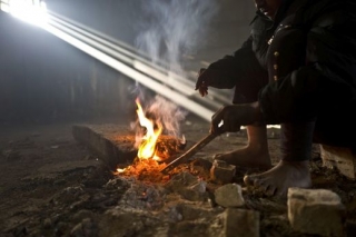 Afghánský uprchlík se zahřívá u ohně.