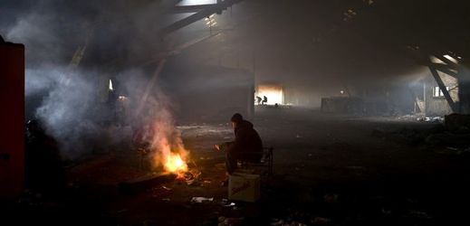 Uprchlík se v opuštěném bělehradském skladišti zahřívá u ohně.
