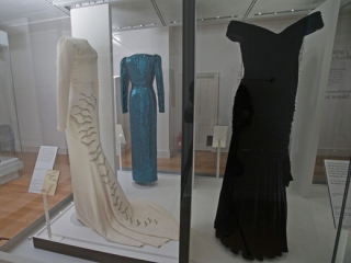 Vlevo hedvábné krémové šaty s flitry navržené Catherine Walkerovou pro princeznu k oficiální návštěvě Saúdské Arábie a vpravo tmavě modré šaty, ve kterých princezna Diana tančila s Johnem Travoltou v Bílém domě v roce 1985.