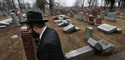 Muž kráčí kolem poničených náhrobků na židovském hřbitově v americkém St. Louis.