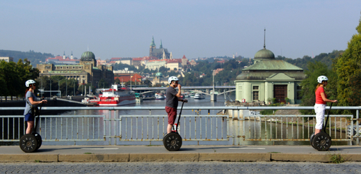 Turisté na vozítkách segway na okružní jízdě Prahou. Snímek z Hlávkova mostu, v pozadí Pražský hrad.