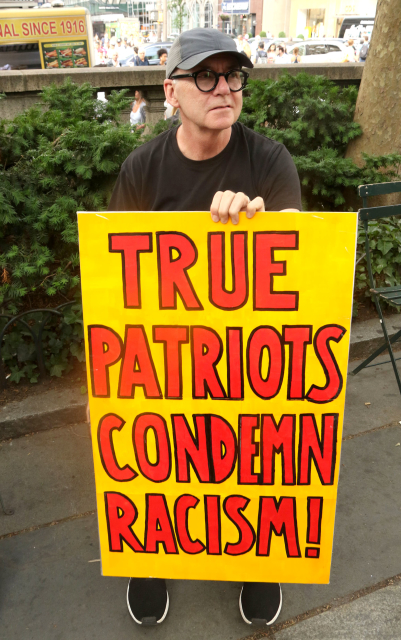 Světový den uprchlíků v New Yorku a muž držící transparent s nápisem: "Opravdoví patrioti pohrdají rasismem." (FOTO: ČTK/ZUMA/Nancy Kaszerman).