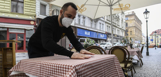 Číšník prostírá stůl na zahrádce restaurace v centru Prahy.
