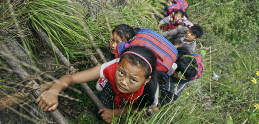 Děti lezoucí po žebříku do svých domovů na útesu.