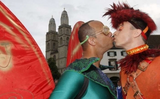 Dva gayové se líbají na pozadí curyšské katedrály.