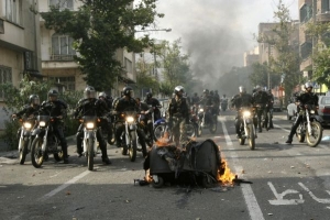 Íránská náboženská milice projíždí kolem hořících trosek.