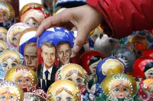 Rusko-americká prezidentská matrjoška. V pozadí vykukuje Putin.