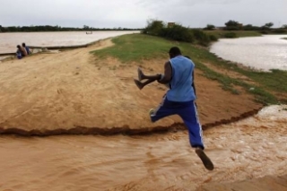 Muž přeskakuje jedno z ramen rozvodněného Nigeru.