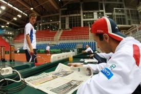 Radek Štěpánek si čte noviny, zatímco Tomáš Berdych trénuje.
