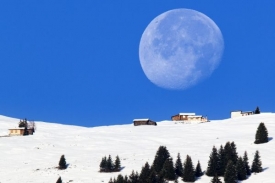 Obrovský měsíc nad zasněženou chatou ve švýcarských Alpách.