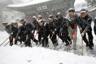 Početná korejská skupinka odklízí hromady sněhu.