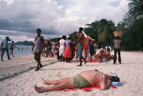 Vykrmený bílý muž se sluní mezi výrazně hubenějšími Haiťany.