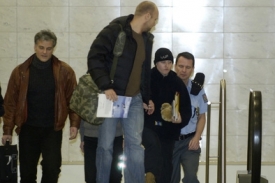 Škrlovou (s kulichem) doprovázejí na letišti v Praze policisté.