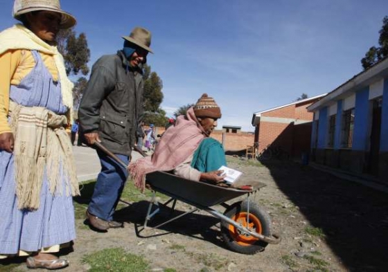 Všichni Indios k urnám. Rodina veze stařenku na vozíku.