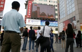 Číňané v ulicích Pekingu sledují přímý přenos z výstupu na Everest.
