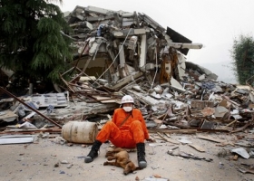 Záchranář odpočívá se svým psem v sutinách po ničivém zemětřesení.
