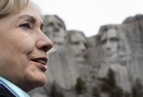 Clintonová u prezidentů USA (Mount Rushmore). Jí se Bílý dům vzdaluje.