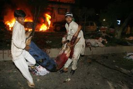 Policisté odnášejí raněného po výbuchu v davu vítajícím Bhuttovou