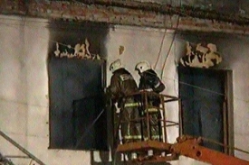 Snímek zachyvuje hasiče, kteří prohlížejí ohořelé trosky domu.