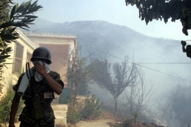 Voják si chrání obličej před kouřem při pokusech uhasit požár v obci Kapsala na řeckém ostrově Evia