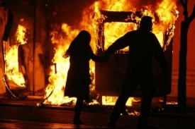 Muž a žena utíkají podél hořící autobusové zastávky v Aténách.