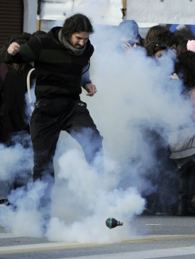 Muž odkopává slzný plyn zpět mezi skupinu policistů.