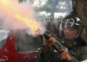 Thajský policista vystřeluje granát se slzným plynem.