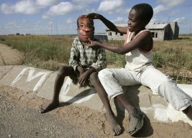 Děti u Harare si hrají s maskou prezidenta Mugabeho.